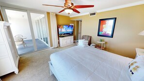 Ein Hotelzimmer mit Bett, Fernseher, Deckenventilator, einem Gemälde und Blick nach außen.