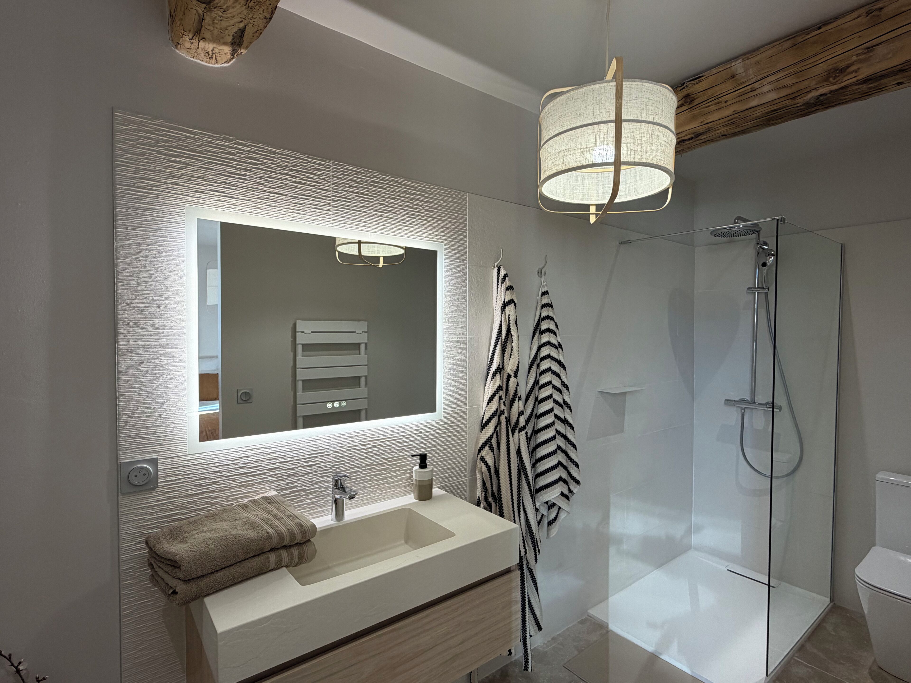 Un baño moderno con un espejo grande, un lavamanos, una ducha y un perchero para toallas.