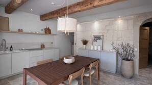 A modern kitchen with a wooden table, white cabinets, and a stone wall. - Petit Mas des Cigales Saint-Rémy de Provence (Saint-Rémy-de-Provence)