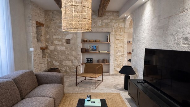 A living room with a sofa, a chair, a coffee table, a TV, and a bookshelf against a stone wall. - Petit Mas des Cigales Saint-Rémy de Provence (Saint-Rémy-de-Provence)