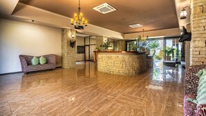 A spacious lobby with a polished wooden floor, a central stone reception desk, and a chandelier. - Simanya River Lodge (Nkurenkuru)