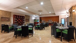 A restaurant with multiple tables and chairs, a wine rack, and a stone wall. - Simanya River Lodge (Nkurenkuru)