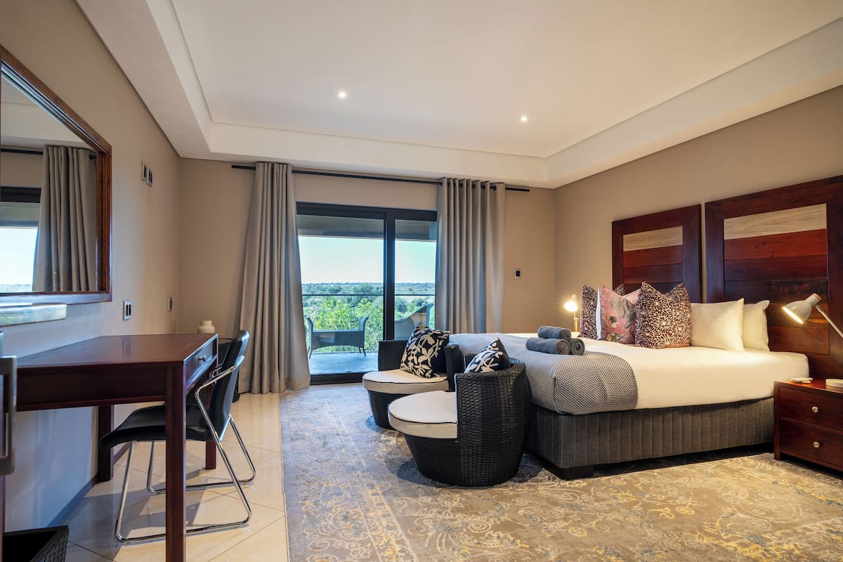 A bedroom with a bed, bedside table, lamp, and a view of the outdoors.