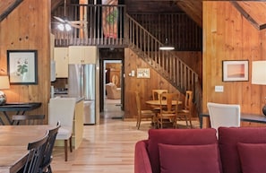 Une pièce spacieuse avec un escalier en bois, un coin repas avec des chaises et une cuisine visible au fond.