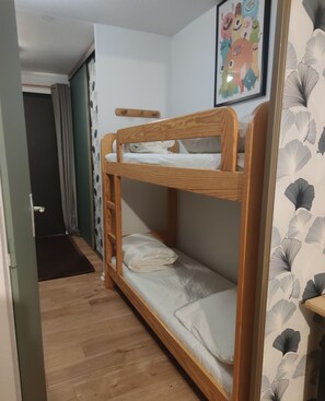 Ein Etagenbett mit Holzrahmen und weißer Bettwäsche, eine Tür mit Fußmatte und eine Wand mit einem gerahmten Bild.