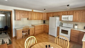 A modern kitchen with wooden cabinets, a dining table with chairs, a refrigerator, a microwave, and an oven. - WATERFRONT ON SAND POND WITH A PRIVATE SANDY BEACH (East Baldwin)