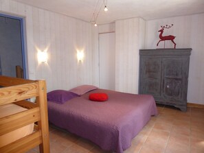 A bedroom with a wooden bed frame, a purple bedspread, and a red pillow. There is a wooden cabinet with a decorative deer sculpture on top. - Luminous gîte surrounded by animals on an organic farm in the Verdon region (Bargème)