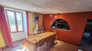 Zona pranzo con tavolo e sedie, cucina con forno a microonde e fornelli, e finestra con tende.