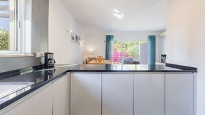 Uma cozinha moderna com bancada preta, armários brancos e uma área de jantar com mesa e cadeiras.