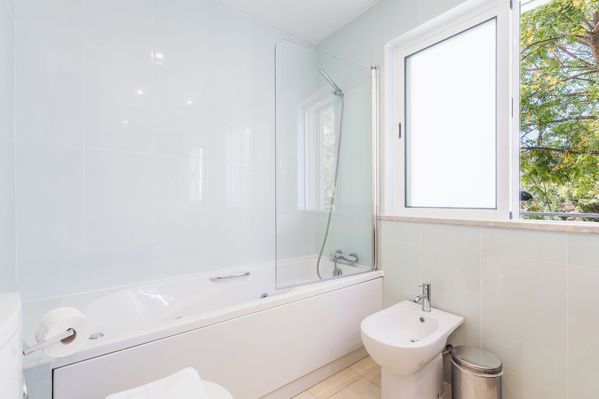 Ein modernes Badezimmer mit einer gläsernen Dusche, einem freistehenden Waschbecken und einem Fenster mit Blick auf Grünflächen.