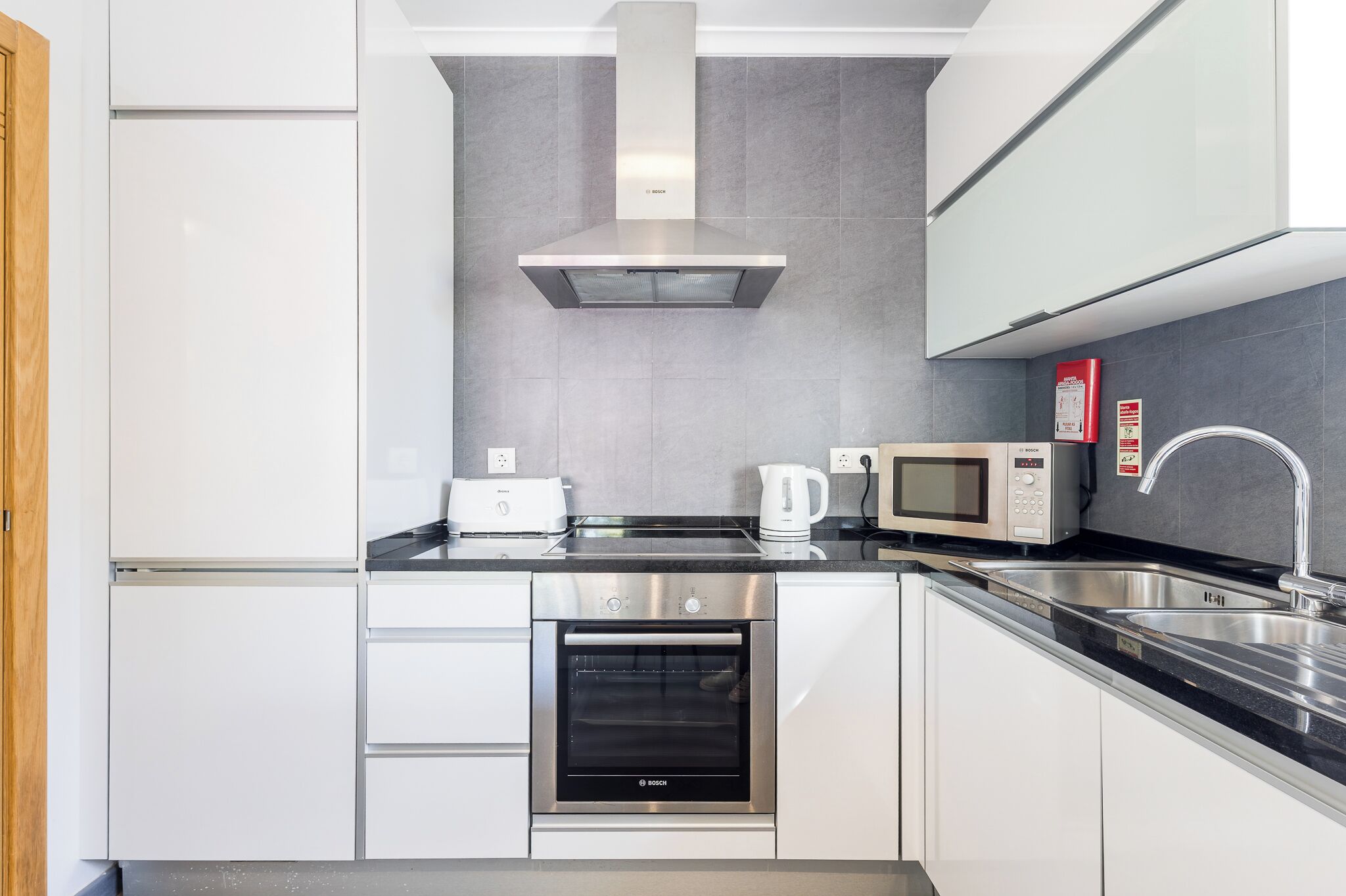 Una cocina moderna con horno Bosch, microondas, hervidor y pileta de acero inoxidable.