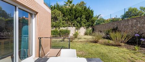 Un patio con una mesa y sillas, un muro de piedra y un área con césped, plantas y flores.