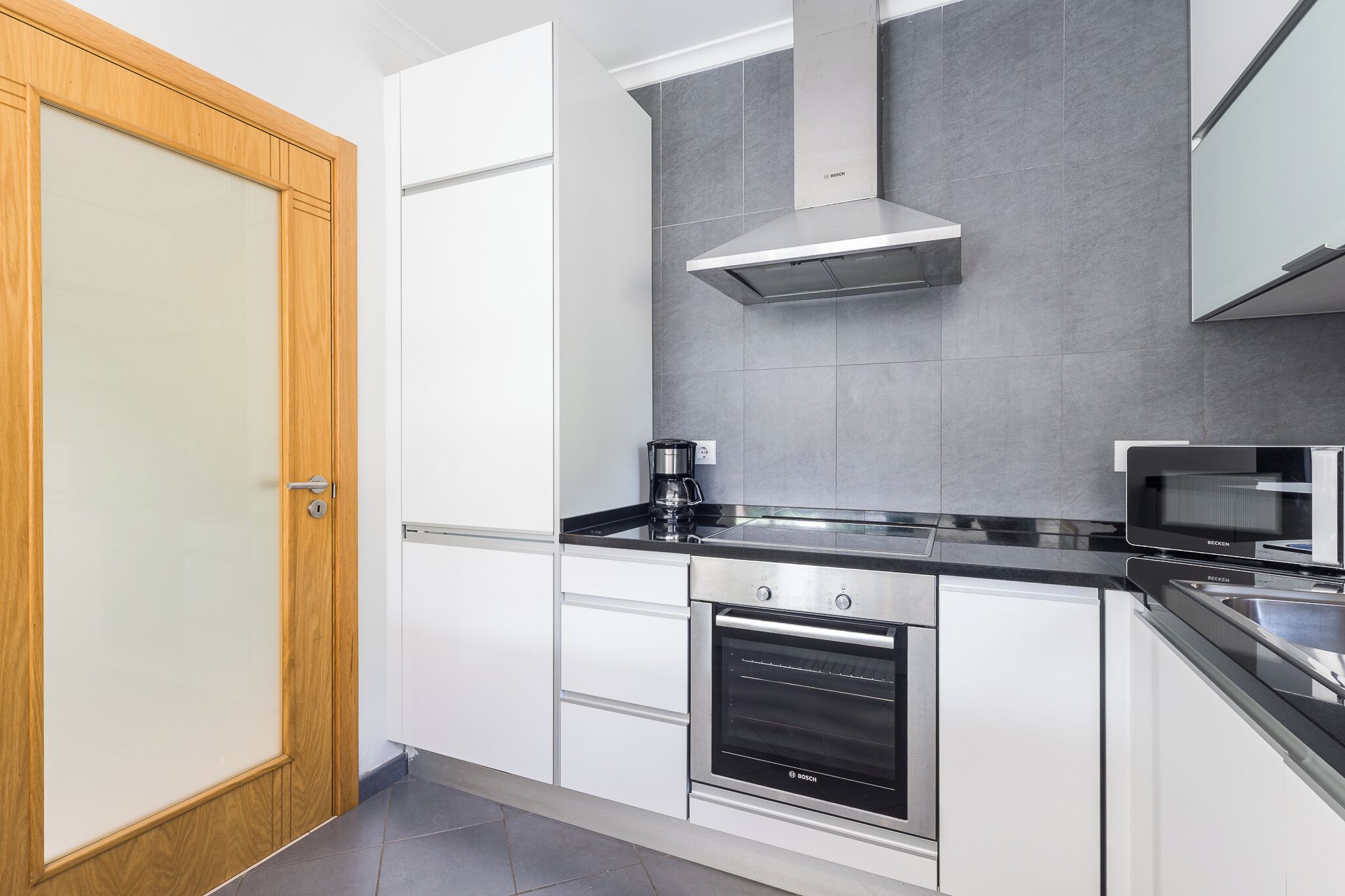 A modern kitchen with white cabinets, a Bosch oven, a microwave, and a coffee maker.