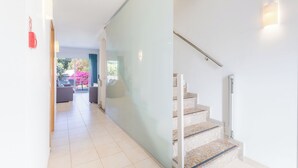 Interior moderno com escada, divisória de vidro e vista para área externa com mobiliário.