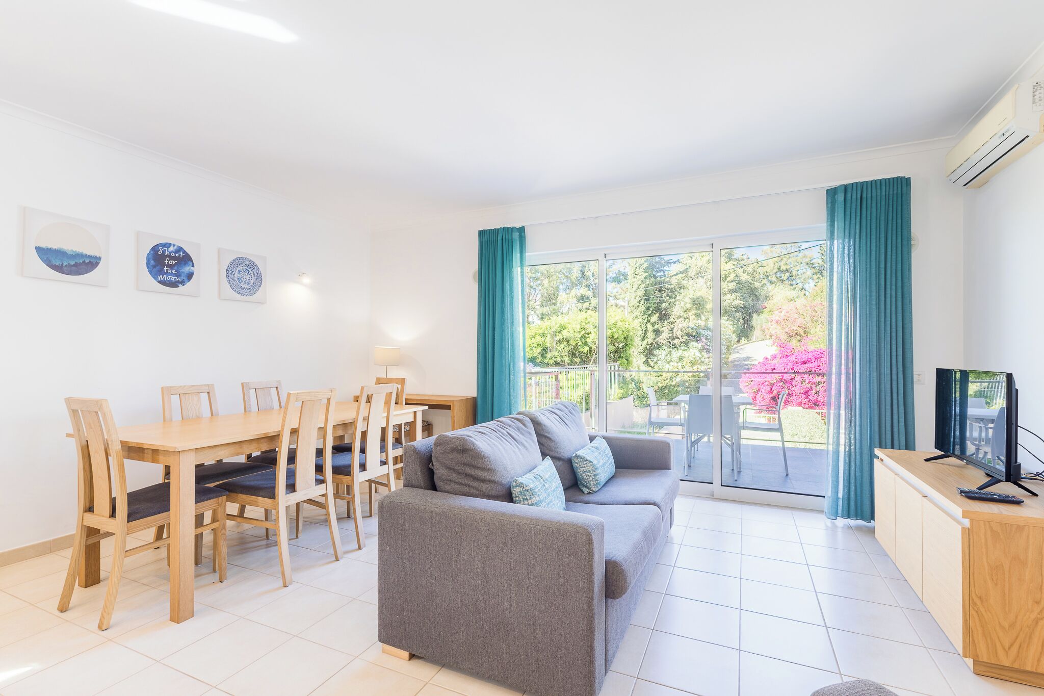 A living room with a sofa, dining table, chairs, a TV, and a sliding glass door to the outside.