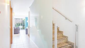 A modern interior with a staircase, a hallway leading to a seating area, and a glass door leading outside.