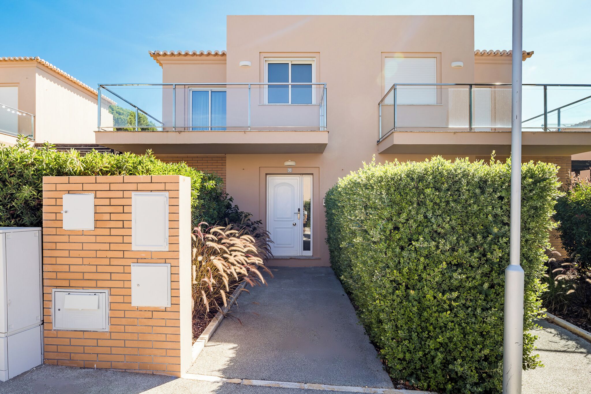 A two-story residential building with a balcony, a door, and a pathway leading to the entrance.