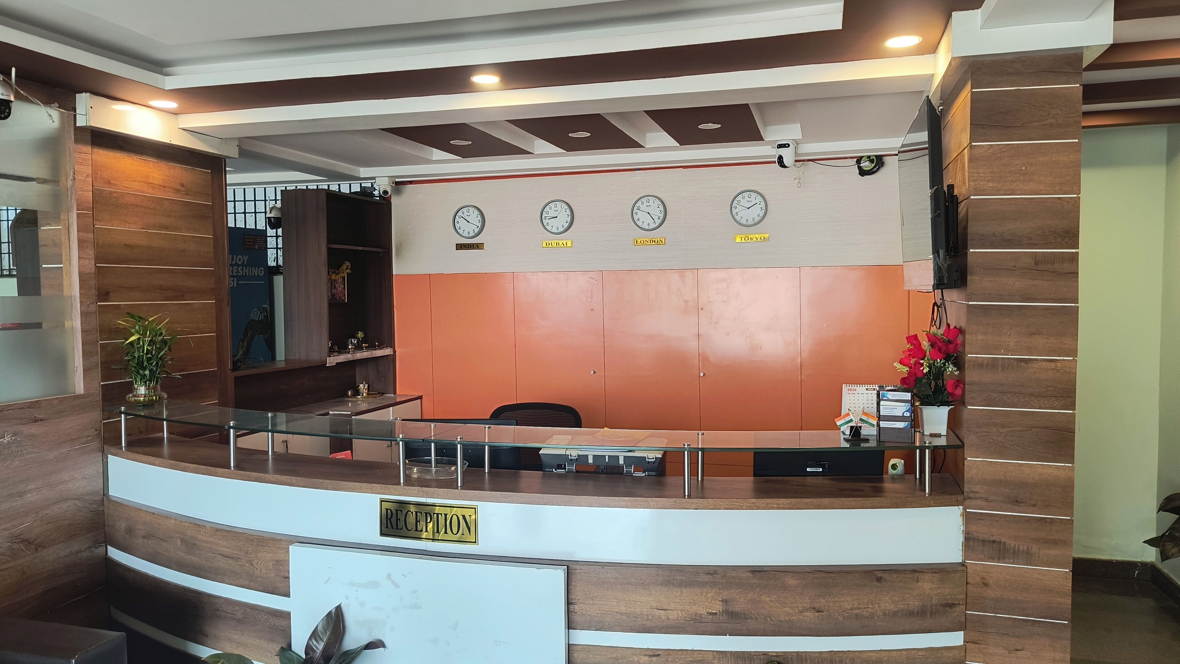 Ein Empfangsbereich mit Glastrennwand, einer Rezeption mit der Beschriftung „RECEPTION“ und Uhren, die die Zeit verschiedener Städte anzeigen.