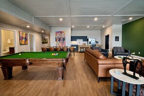 A pool table, a sofa, a dining area, and a kitchen in a modern interior. - NuLu 6BR Penthouse | Hot Tub w/City Views | Kings (Louisville)