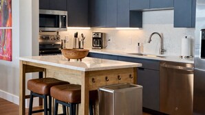 Une cuisine moderne avec des meubles bleu foncé, des appareils en acier inoxydable, un plan de travail en marbre et un saladier en bois servant de centre de table.