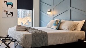 Une chambre à coucher moderne avec un lit, des oreillers, une couverture, une lampe fixée au mur et des œuvres d’art représentant des chevaux.