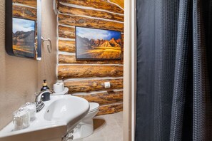 A bathroom with a rustic wooden wall, a sink, toilet, and two framed pictures. - Pinecrest Cabin: Central Black Hills Getaway (Rapid City)