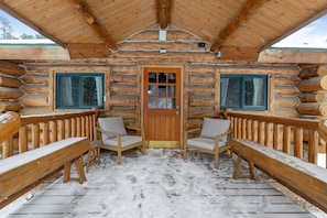 Una cabaña de troncos con una terraza de madera, dos sillas y una puerta.