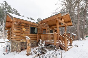 A log cabin with a stone foundation, wooden exterior, and a porch with a metal railing. - Pinecrest Cabin: Central Black Hills Getaway (Rapid City)