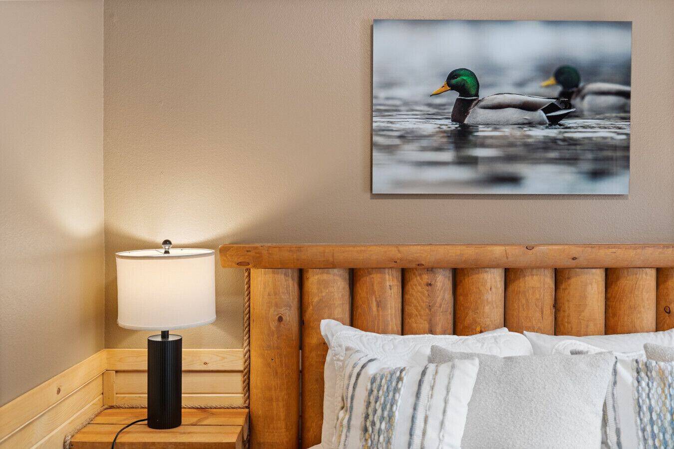 Ein Schlafzimmer mit einem Holzkopfteil, einem Nachttisch mit Lampe und einem Bilderrahmen mit Enten an der Wand.