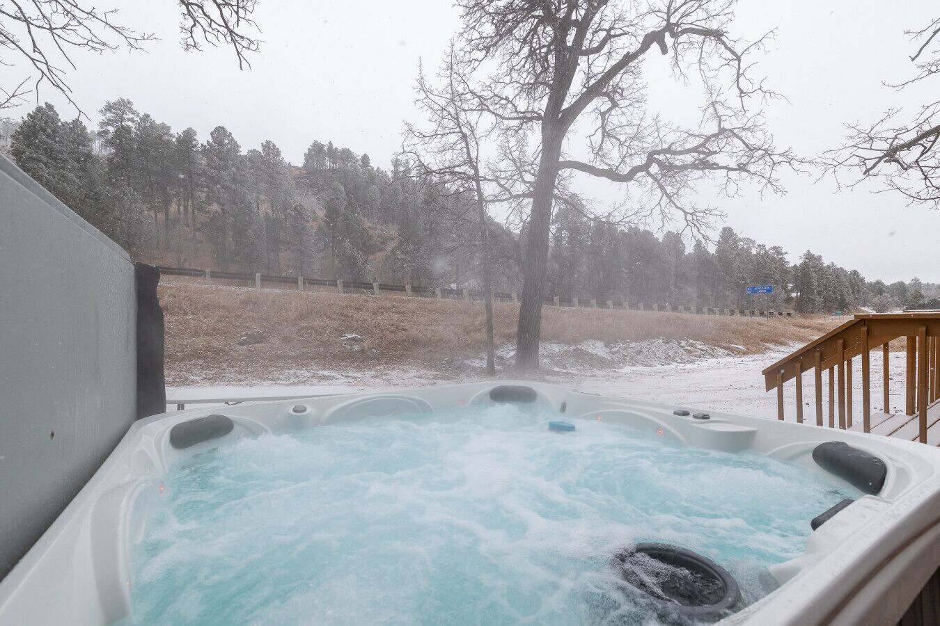 Un bain à remous doté d’une terrasse en bois et offrant une vue sur un paysage enneigé parsemé d’arbres.