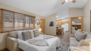 A cozy bedroom with a large bed, a sitting area with a sofa, and a view of the kitchen and living area.
