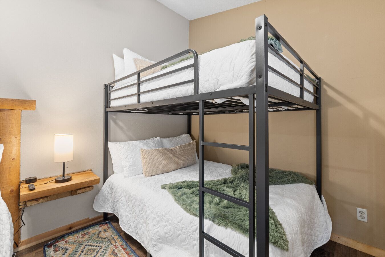 A bunk bed with a wooden headboard, a bedside table with a lamp, and a patterned rug.