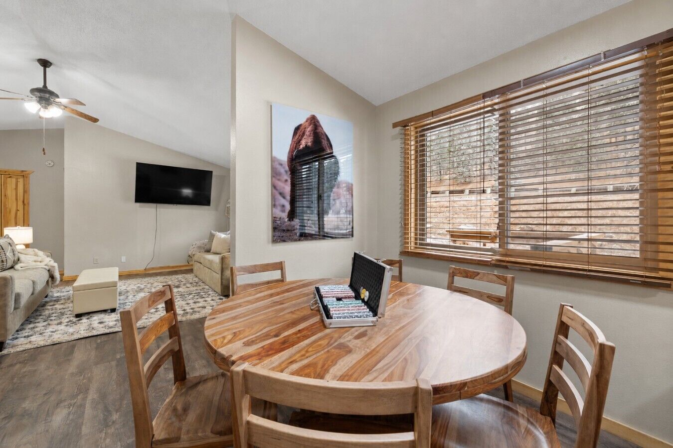 Un'area pranzo con un tavolo rotondo in legno, sei sedie, una ventola a soffitto, una TV a schermo piatto e una finestra con persiane.