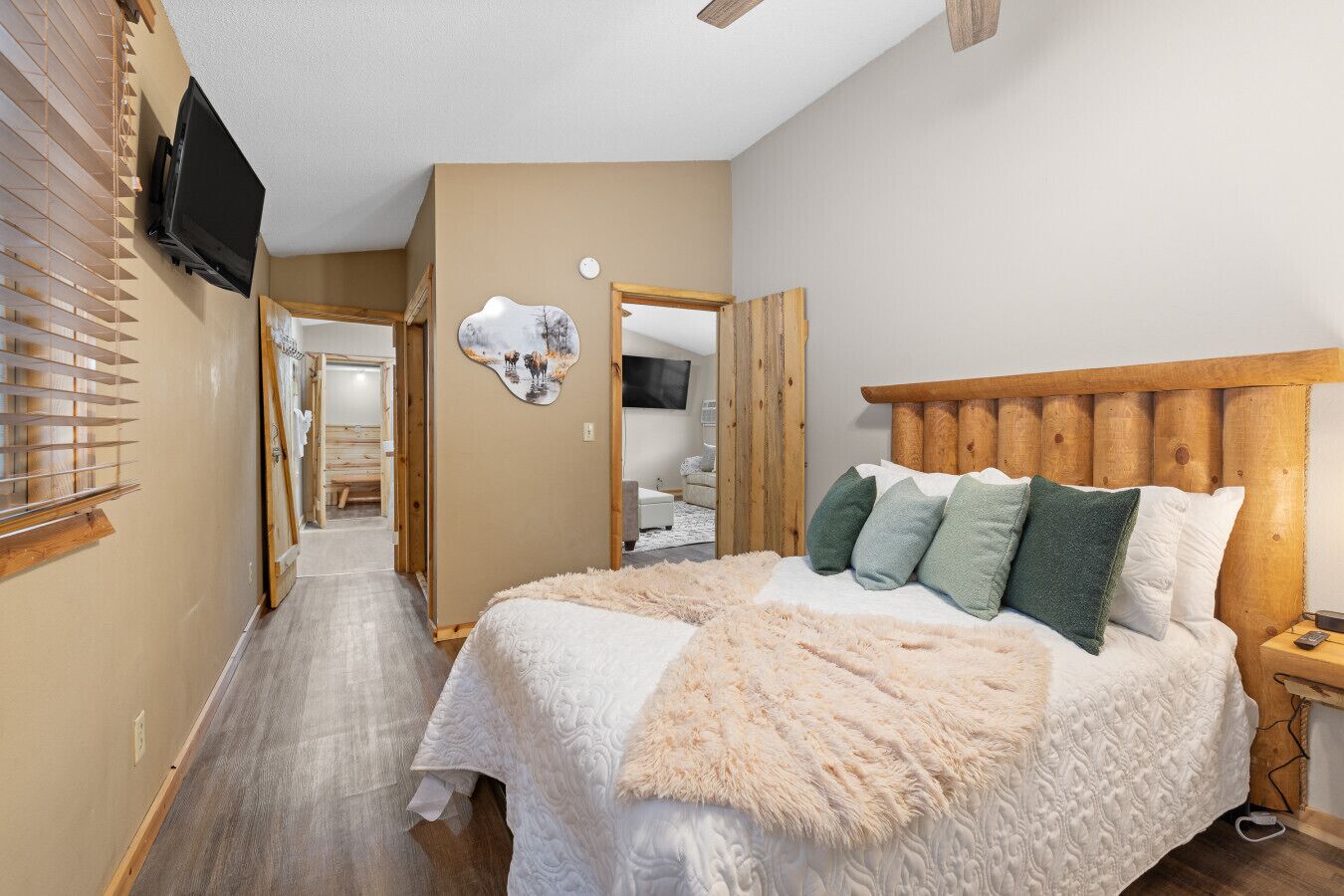 A bedroom with a wooden headboard, a large bed with multiple pillows, a fluffy throw blanket, and a wall-mounted TV.