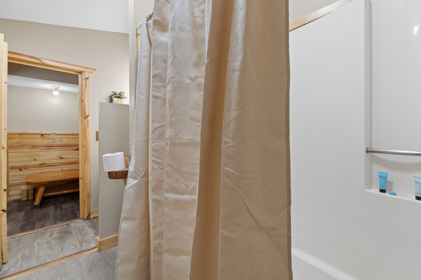 A bathroom with a wooden bench, a shower curtain, and toiletries on the wall.
