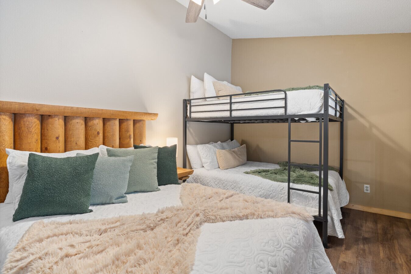 Une chambre avec un lit superposé, une tête de lit en bois, un plaid beige moelleux et plusieurs oreillers.