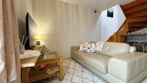 A living room with a sofa, a coffee table, a TV, and a staircase leading to a dining area. - Apartment 5 minutes from Decathlon Arena, including secure parking. Free shuttle (Villeneuve-d'Ascq)