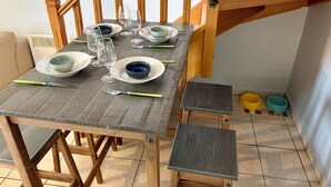 Uma mesa de jantar posta com pratos, tigelas e talheres, acompanhada por um banquinho e uma cadeira.