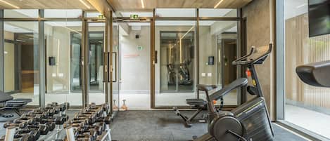Ein Fitnessstudio mit Trainingsgeräten, darunter Kurzhanteln und ein Crosstrainer.