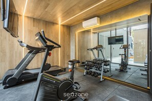 Une salle de sport équipée de tapis de course, d’un appareil elliptique et d’une série de haltères.