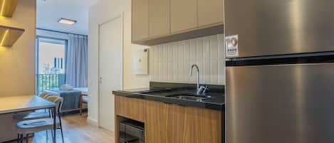 Eine kleine Küche mit einem Edelstahl-Kühlschrank, einem Einbauofen und einem Spülbecken mit Armatur.