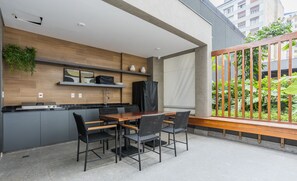An outdoor kitchen area with a dining table and chairs, a built-in stove, and a view of a garden through a wooden railing. - Studio in Condo w/ Gym in Consolacao Mac0046 (São Paulo)