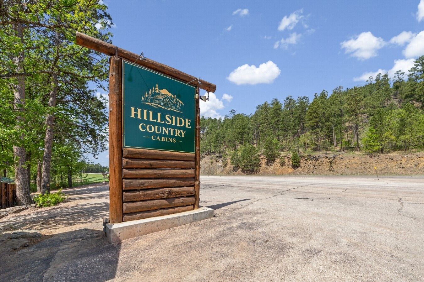 Señal de Hillside Country Cabins, con una estructura de madera y una vista despejada del bosque circundante.