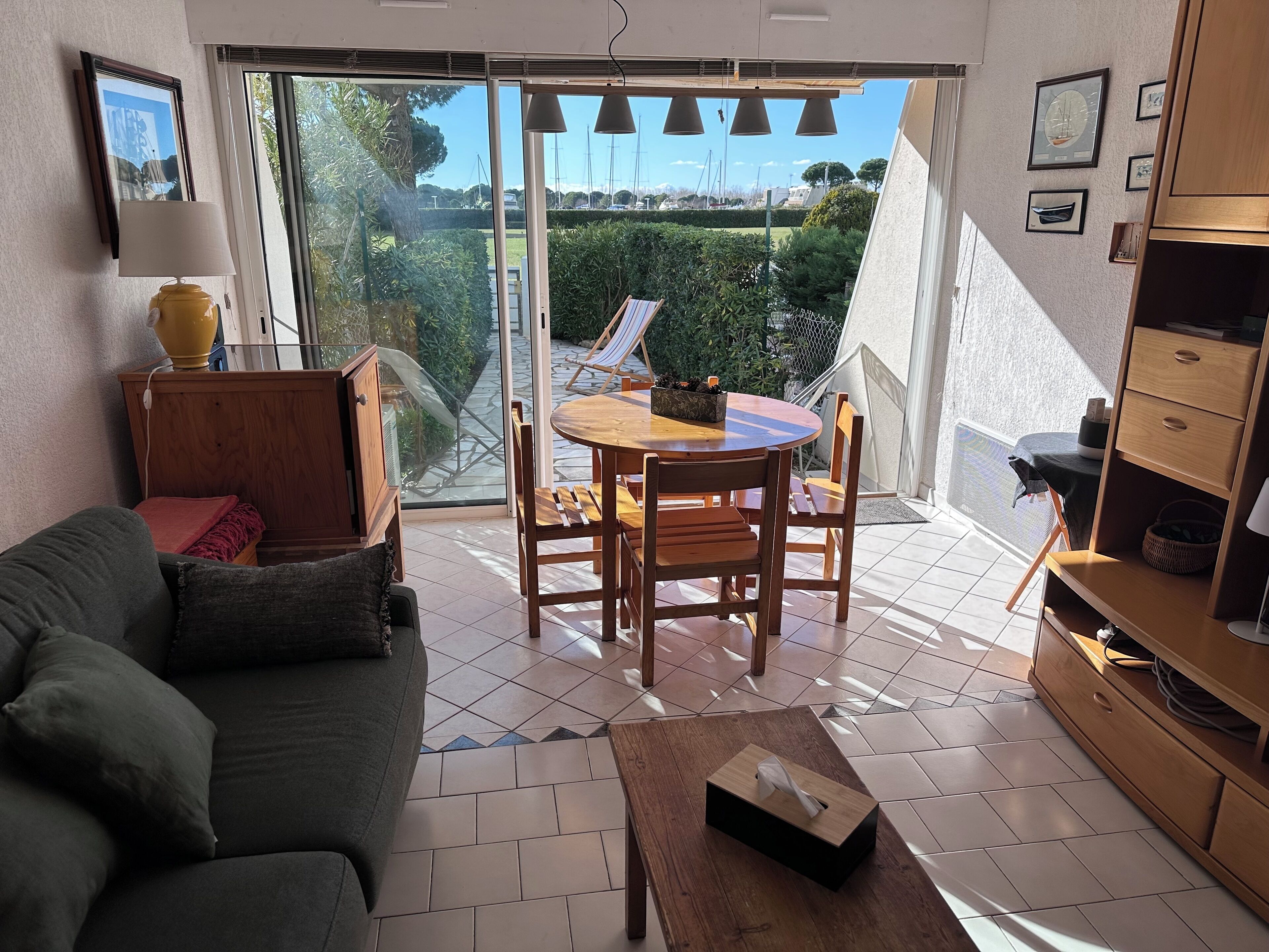 A living room with a sofa, a wooden table, and a balcony with a view of greenery and boats.