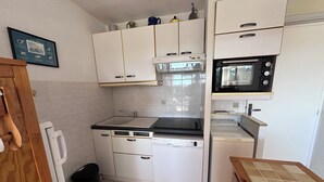 A compact kitchen with white cabinets, a black countertop, a microwave, a stove, and a dishwasher. - RESIDENCE L'ISLE CATHERINE BEL APPARTEMENT 2 PIECES RDC JARDIN PRIVATIF PK ET CLIM (Le Grau-du-Roi)