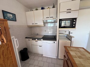 A compact kitchen with white cabinets, a black countertop, a microwave, a stove, and a dishwasher. - RESIDENCE L'ISLE CATHERINE BEL APPARTEMENT 2 PIECES RDC JARDIN PRIVATIF PK ET CLIM (Le Grau-du-Roi)