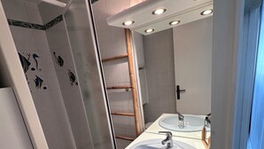 A modern bathroom with a white sink, mirror, and shower. - RESIDENCE L'ISLE CATHERINE BEL APPARTEMENT 2 PIECES RDC JARDIN PRIVATIF PK ET CLIM (Le Grau-du-Roi)