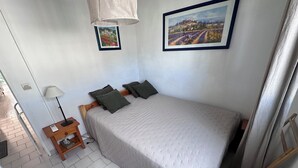 A bedroom with a bed, a nightstand, a lamp, and two framed pictures on the wall. - RESIDENCE L'ISLE CATHERINE BEL APPARTEMENT 2 PIECES RDC JARDIN PRIVATIF PK ET CLIM (Le Grau-du-Roi)