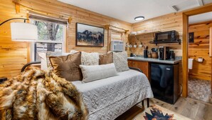 L’intérieur chaleureux d’un chalet comprend un lit, un bureau, un four à micro-ondes et une fenêtre donnant sur une forêt.