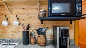 Une cuisine compacte équipée d’un four à micro-ondes, d’une machine à café et d’ustensiles de cuisine en bois, le tout posé sur le plan de travail.